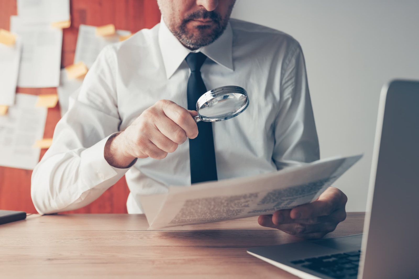 A buyer examining a printed document with a magnifying glass at an office desk