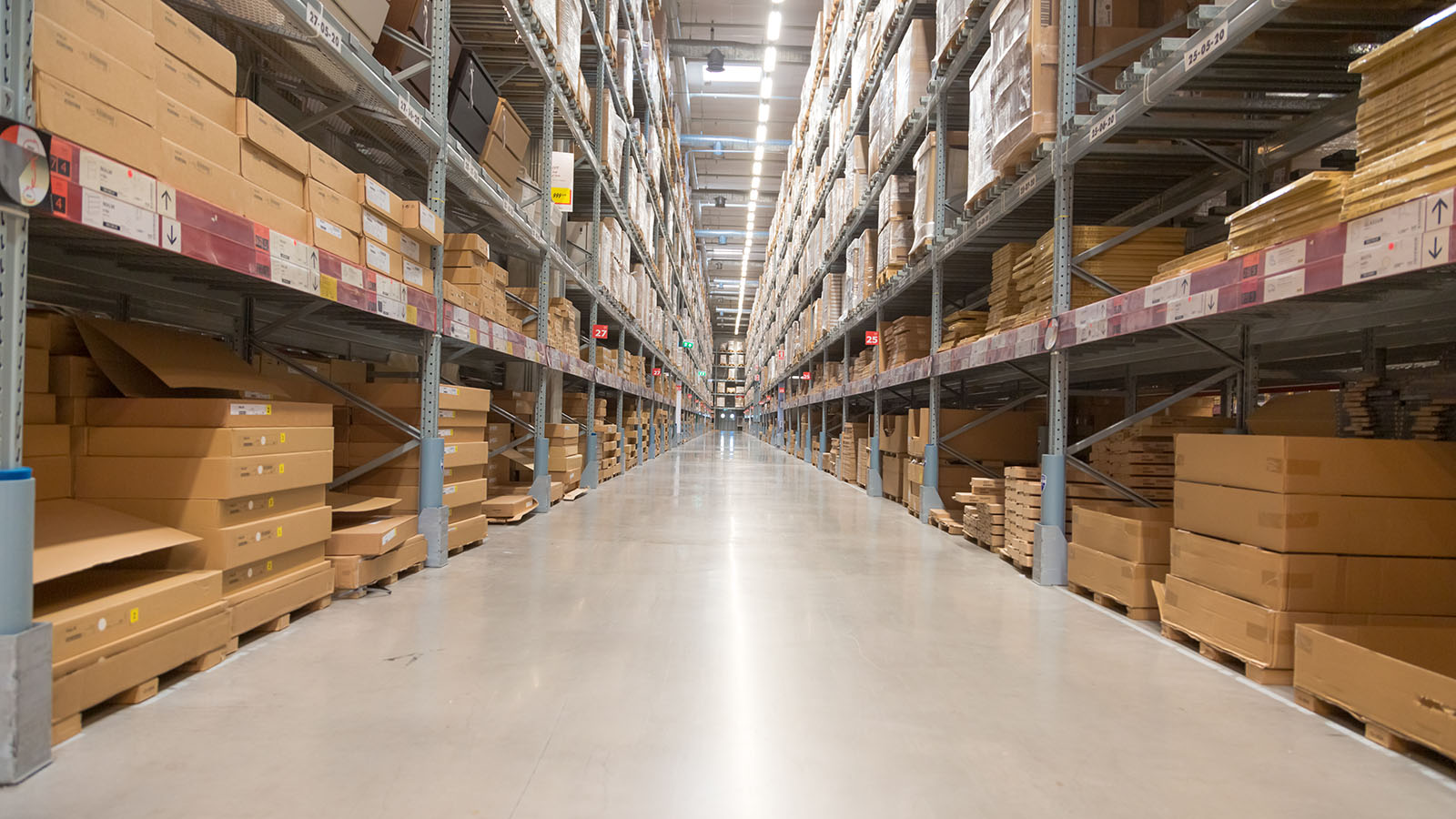 Long warehouse aisle lined with racking full of stacked cartons ready for distribution