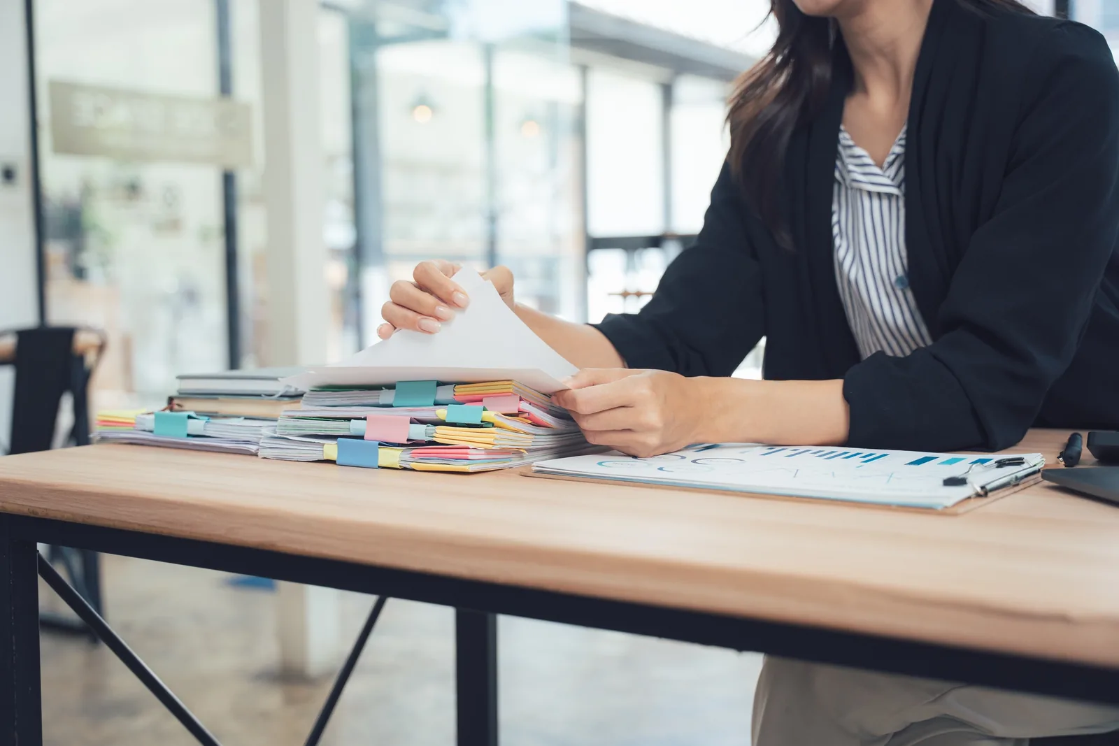 Person reviewing a stack of tabbed documents and a printed chart at a wooden desk
